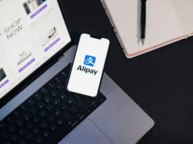 Smartphone displaying Alipay app on open laptop with online shopping site.