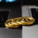 Close-up of gold Bitcoin coins placed on laptop keyboards, representing digital currency and wealth.