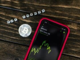 Smartphone showing bitcoin price with a physical coin and text representing cryptocurrency investment.