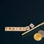 Bitcoin and trading concept shown with coins, pen, and letter tiles on a dark background.