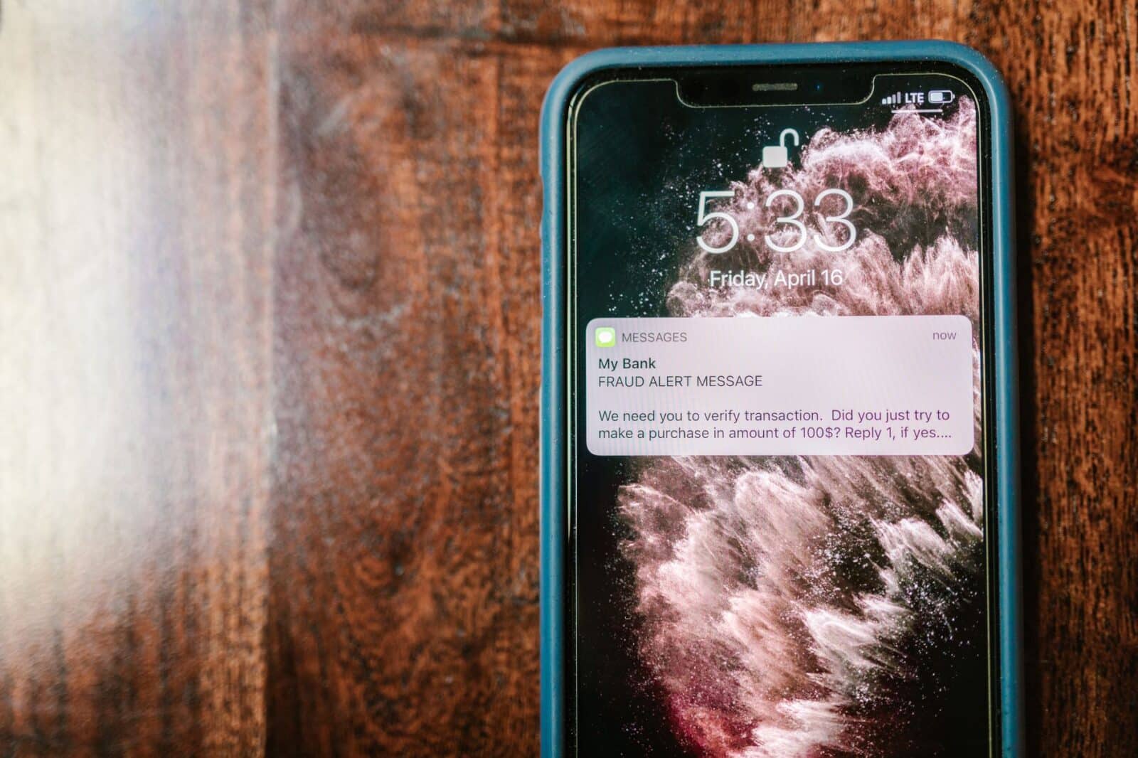Close-up of a smartphone displaying a fraud alert notification on a wooden surface.
