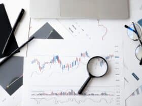 Flat lay of stock market analysis documents with magnifying glass, pens, and glasses.