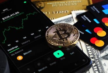 Bitcoin coin with financial data, credit cards, and currency on a desk.