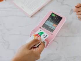 Hand using a contactless card on a pink POS terminal for a wireless transaction.