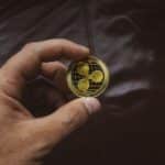A close-up of a hand holding a gold Ripple cryptocurrency coin, symbolizing digital currency concept.
