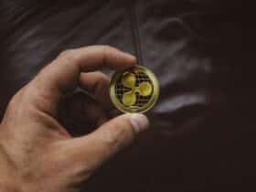 A close-up of a hand holding a gold Ripple cryptocurrency coin, symbolizing digital currency concept.