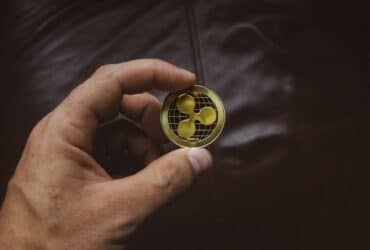 A close-up of a hand holding a gold Ripple cryptocurrency coin, symbolizing digital currency concept.