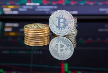 Bitcoin coins stacked in front of cryptocurrency trading chart reflecting market trends.