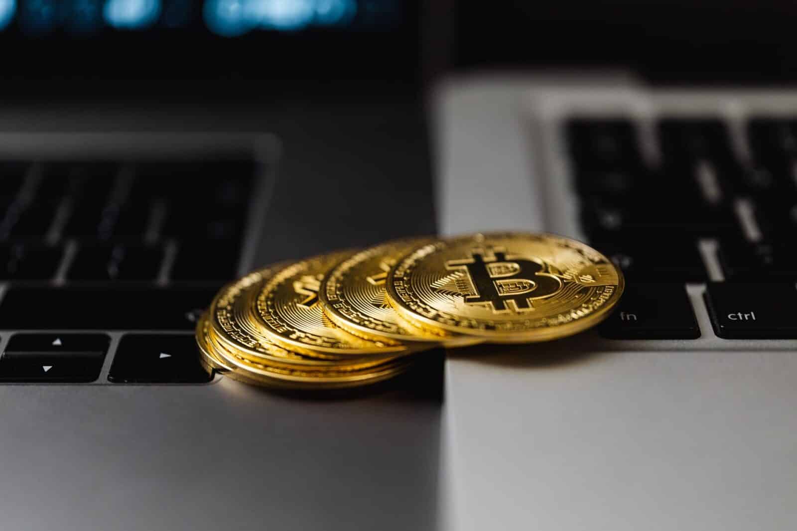Close-up of gold Bitcoin coins placed on laptop keyboards, representing digital currency and wealth.
