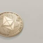 A golden Ethereum coin placed on a neutral light background, symbolizing digital currency.