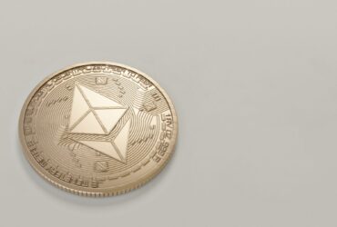 A golden Ethereum coin placed on a neutral light background, symbolizing digital currency.
