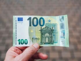 Close-up photo showing a person holding a 100 euro banknote against a blurred background.