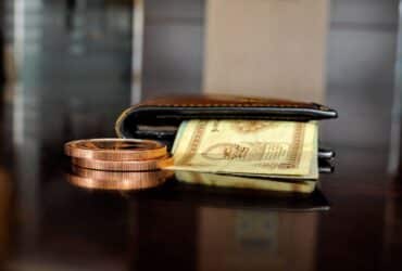 Arrangement of antique coins and banknotes beside a wallet, reflecting luxury finance.