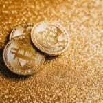 Closeup of three Bitcoin coins on a shimmering gold glitter background, symbolizing digital wealth.