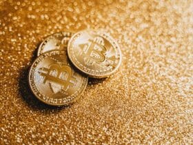 Closeup of three Bitcoin coins on a shimmering gold glitter background, symbolizing digital wealth.