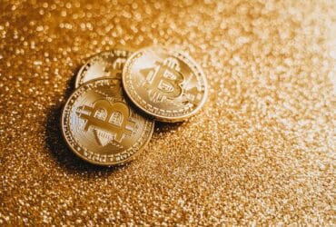 Closeup of three Bitcoin coins on a shimmering gold glitter background, symbolizing digital wealth.