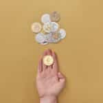 Close-up of a hand holding a cryptocurrency coin on a yellow background with scattered coins.