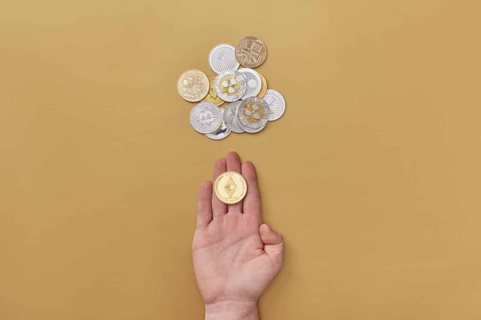 Close-up of a hand holding a cryptocurrency coin on a yellow background with scattered coins.
