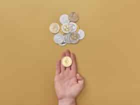 Close-up of a hand holding a cryptocurrency coin on a yellow background with scattered coins.